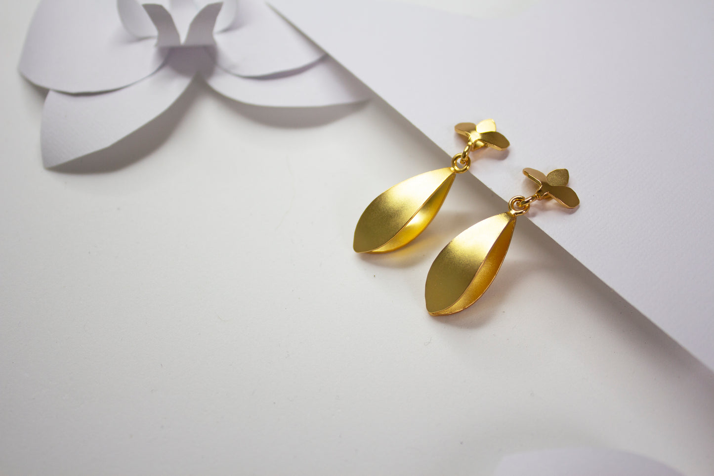 Iris Golden earrings on a white surface with a decorative bow in the background