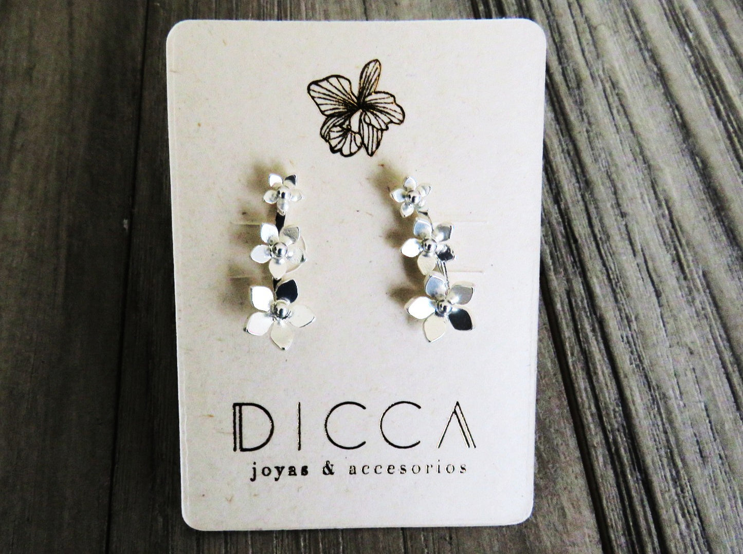 Guayacan. Silver floral earrings on a DICCA branded card against a wooden background