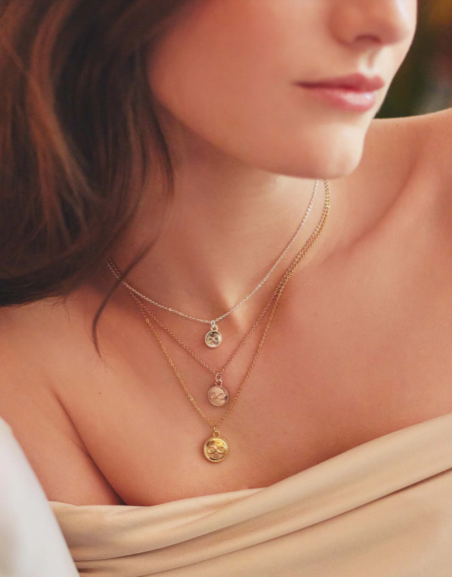 A person wearing a set of three layered necklaces with pendant charms, in gold, silver, and rose gold colors.