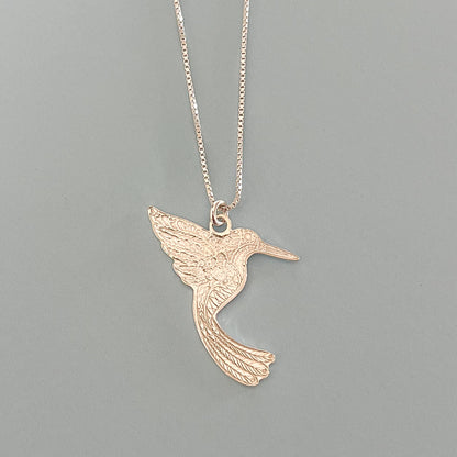Silver hummingbird pendant necklace on a gray background