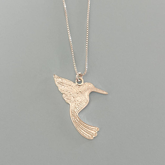 Silver hummingbird pendant necklace on a gray background