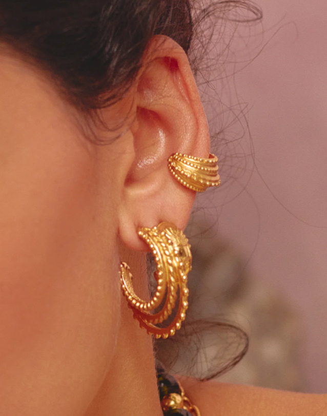 Close-up of a person wearing gold hoop earrings with a blurred background