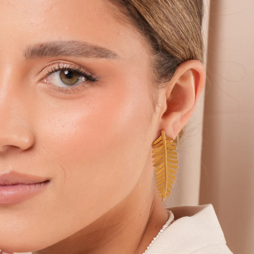 Close-up of a woman wearing golden fern-shaped earrings with a neutral background