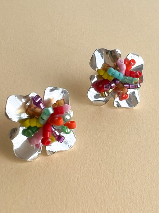 Silver flower-shaped earrings with colorful beads on a beige background