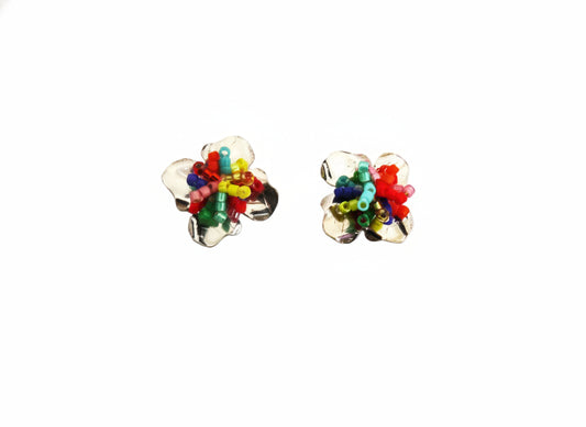 Colorful flower-shaped earrings on a branded card with 'Andrea Montoya' on a wooden surface.