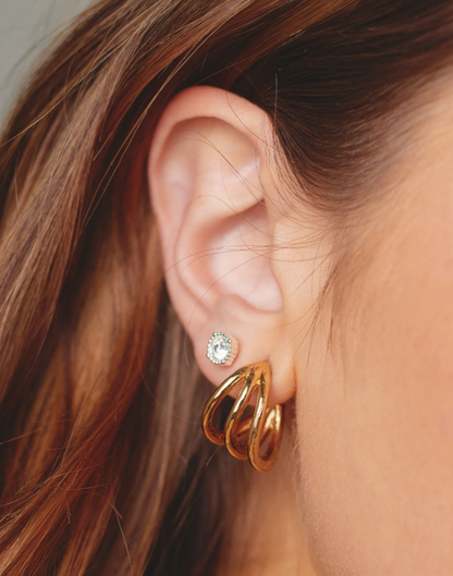 A close-up image of a woman's ear wearing a gold hoop earring with a small stud earrings also visible.