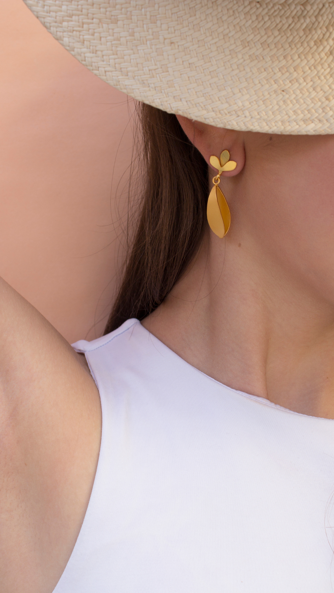 Close-up of a person wearing Iris golden earring with a white top and beige hat.