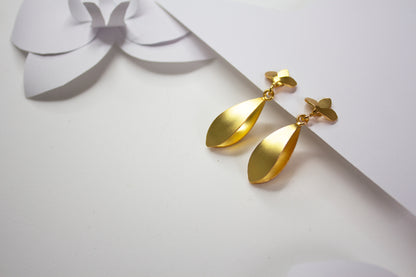 Iris Golden earrings on a white surface with a decorative bow in the background