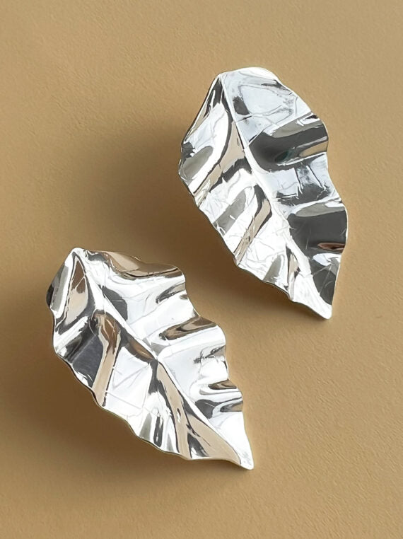 Silver leaf-shaped earrings on a beige background