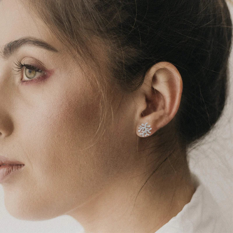 Close-up of a woman wearing a silver earring with a coral design.