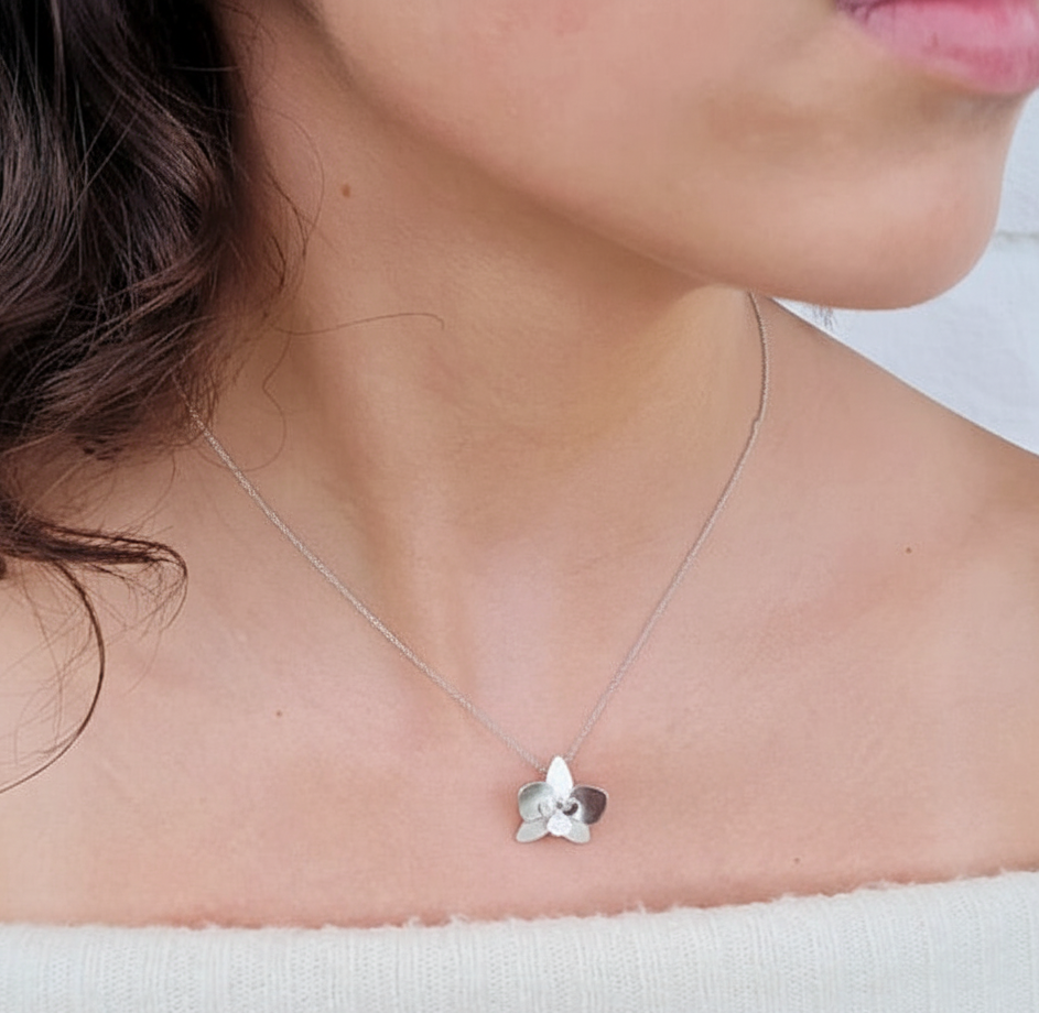 Silver necklace with a orchid flower pendant worn by a person