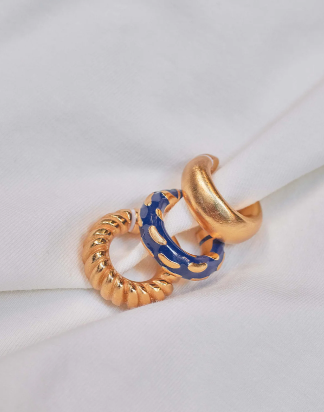 A set of three earcuffs in gold and blue colors placed on a white surface.