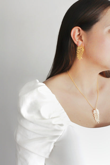 Woman wearing Palm Golden Earrings and necklace on a plain background