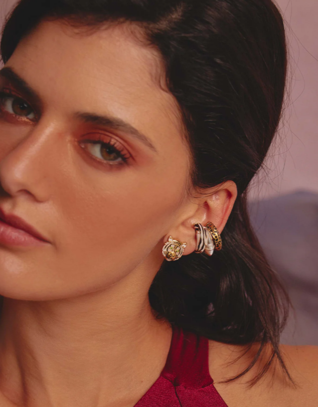A person wearing a set of three gold-colored earcuffs with a safari-inspired design.